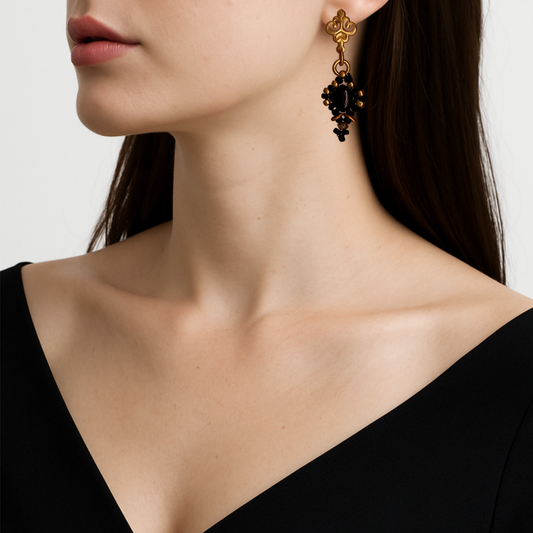 Close-up of a woman wearing a gold tone earring with black stones on a neutral background