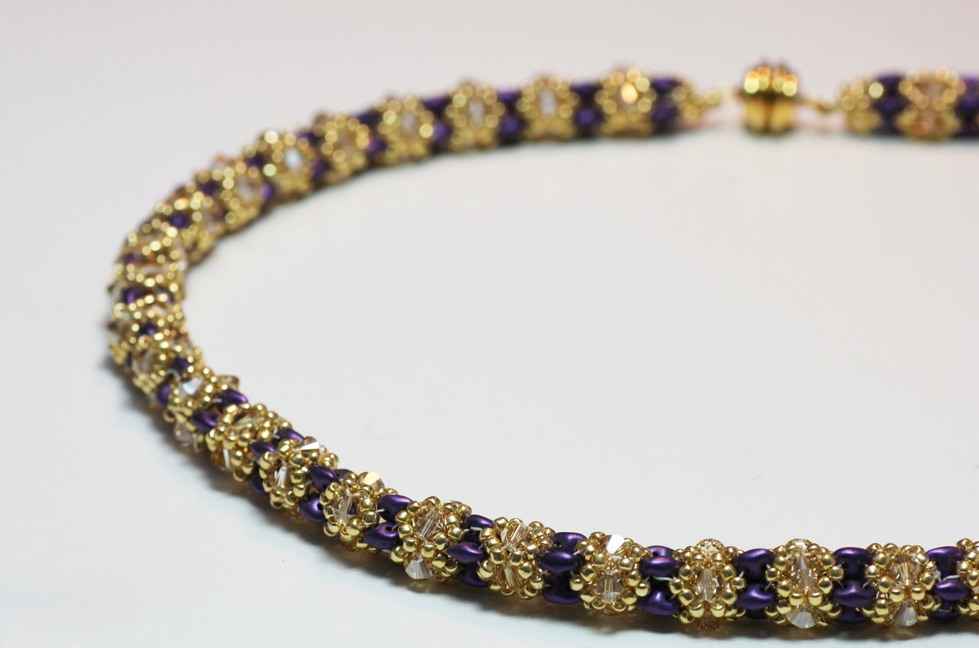 Handmade beaded necklace in gold and violet tones, floral pattern, on white background close up