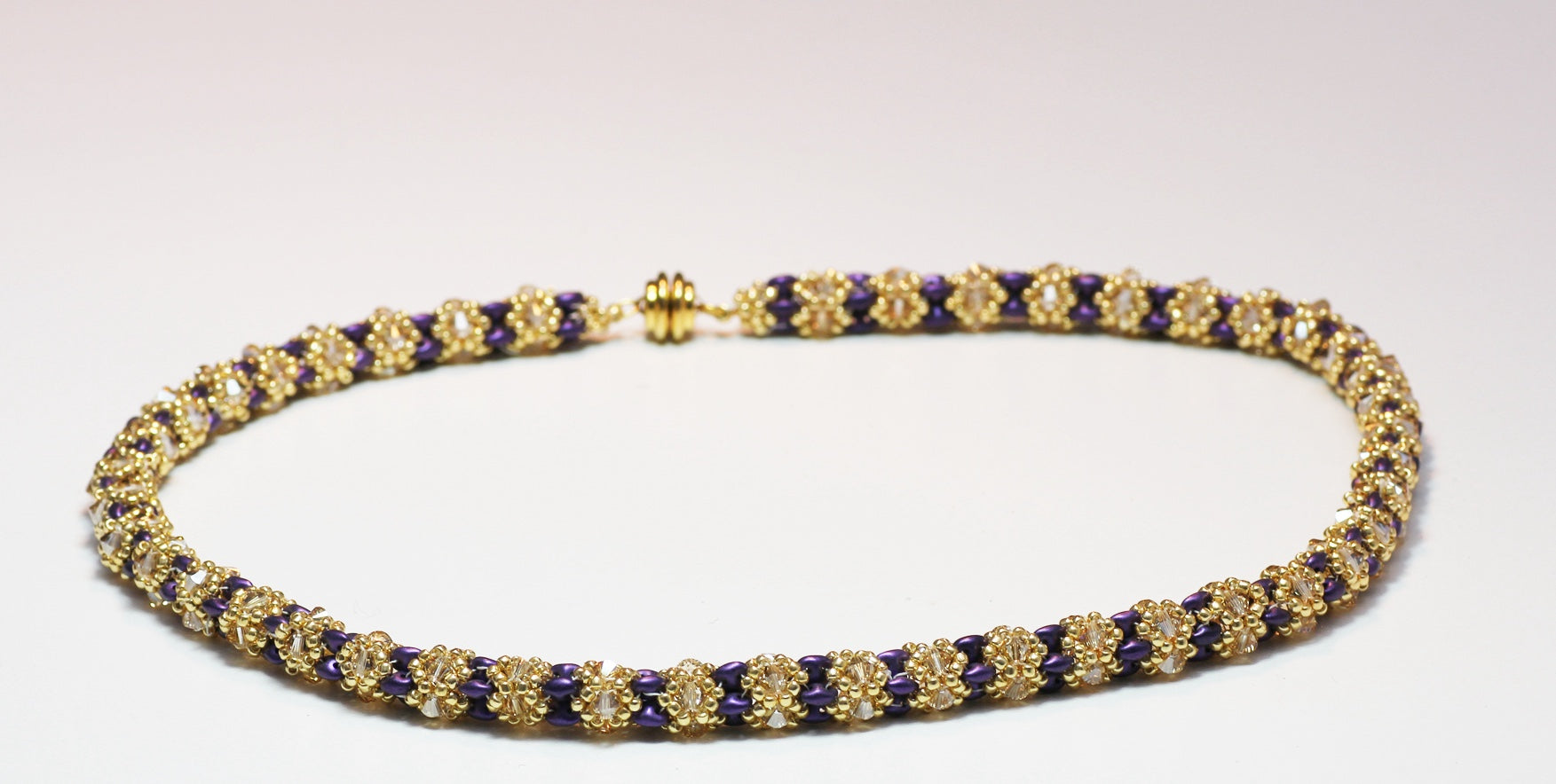 Handmade beaded necklace in gold and violet tones, floral pattern, on white background on full close up